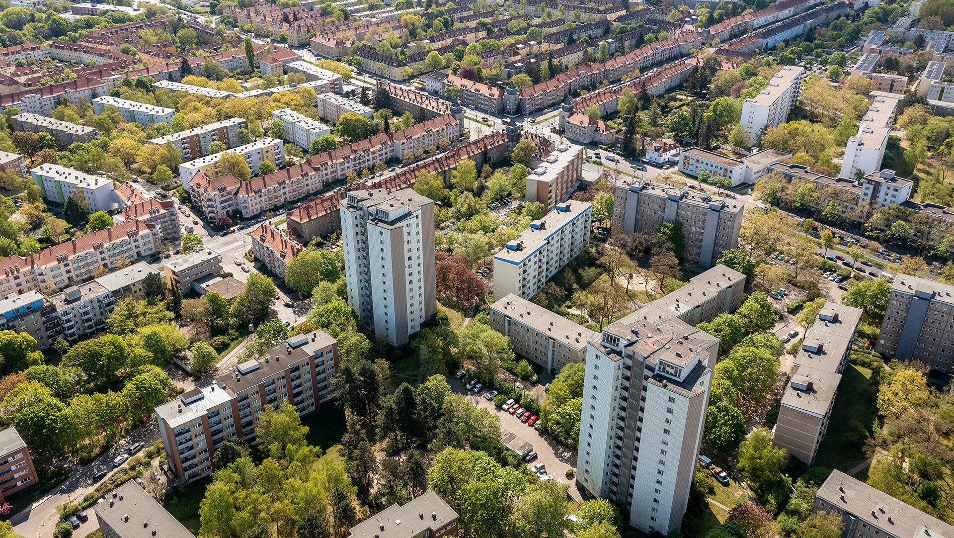 Berlin von schräg oben mit mehreren Hochhäusern, weiteren Häusern, Straßen, Autos und grünen Bäumenn