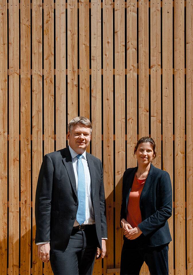Nadine Stelter von der Landesbank Baden-Württemberg, Expertin für Immobilienfinanzierungen, und Bereichsleiter Financial Services, Dr. Thorben Lubnau, stehen gemeinsam vor einer mit Holz verkleideten Wand.